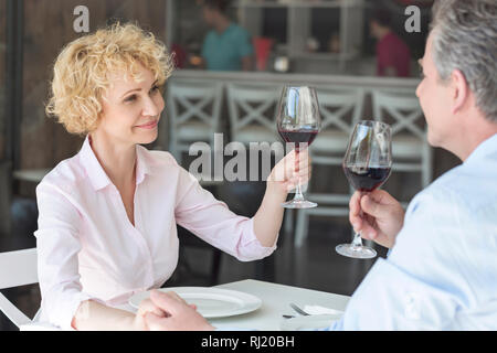 Lächelnd reifes Paar toasten Weingläser beim Sitzen am Tisch im Restaurant Stockfoto