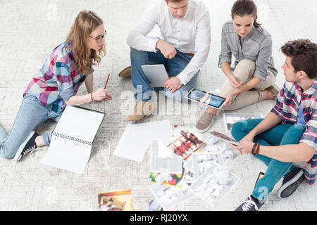 Kollegen diskutieren über Fotos beim Sitzen auf dem Boden Stockfoto