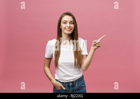 Foto der glückliche junge Frau stehen und poiting Finger über rosa Hintergrund isoliert. Stockfoto