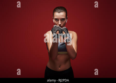 Junge hübsche Sportlerin workout Handschuhe zu tragen bereit ist, einen Gegner zu kämpfen. Über den roten Hintergrund isoliert Stockfoto