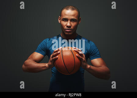 Portrait von stattlichen Athleten im blauen T-Shirt und schwarze Shorts über dunklen Hintergrund isoliert stehen und von der Kamera Stockfoto