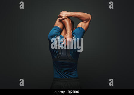 Portrait von starke junge muskulöse Mann seine Arme ausdehnen. Fitness afrikanischen männliches Modell stehen über dunklen Hintergrund. Ansicht von hinten