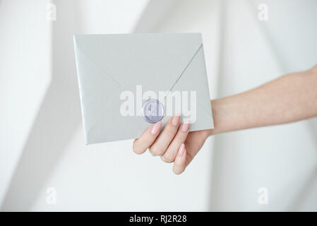 Nahaufnahme von weiblichen Händen hält einen silbernen Einladung Umschlag mit einem Wachs Dichtung, ein Geschenkgutschein, eine Postkarte, eine Hochzeit Einladungskarte Stockfoto