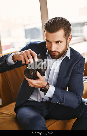 Auf der Suche nach Inspiration. Charmante junge Unternehmer ist die Bilder auf der Kamera während der Sitzung auf Büro Sofa. Business Look. Close-up Stockfoto