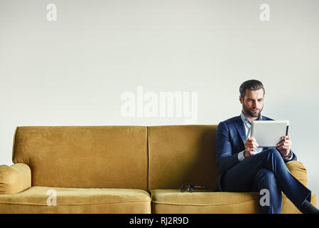 Multitasking... Besetzt Geschäftsmann arbeitet mit Touchpad beim Sitzen auf der Couch im Büro. Business Look. Stockfoto