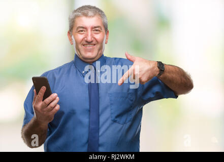 Gut aussehender älterer Mann sms senden Nachricht mit Smartphone über isolierte Hintergrund mit Überraschung Gesicht zeigenden Finger zu sich selbst Stockfoto