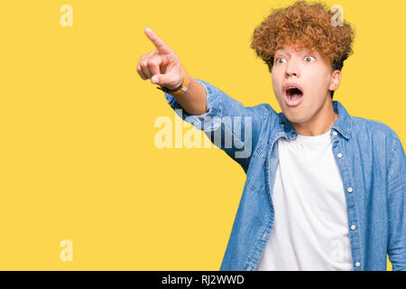 Junger stattlicher Mann mit afro Haar Jeansjacke zeigte mit dem Finger vor überrascht, offenem Mund erstaunt Ausdruck, etwas vor Stockfoto