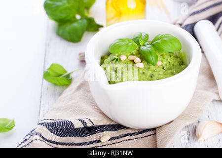 Hausgemachte, traditionelle Basilikum Pesto mit Olivenöl, zeder Muttern und Knoblauch in einer weißen Schüssel auf einem hölzernen rustikalen Tisch, Nahaufnahme Stockfoto