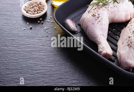 Raw Hähnchenschenkel mit Kräutern, Knoblauch und Tomaten, bereit, auf einen schwarzen Stein Hintergrund zu kochen, Nahaufnahme Stockfoto