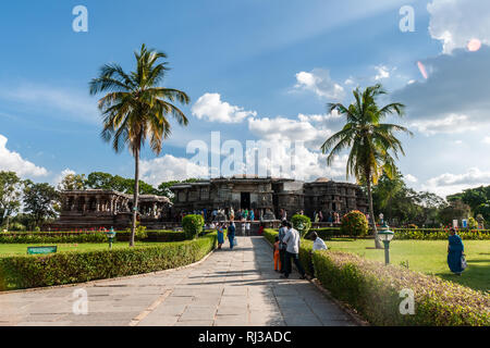 Halebidu, Karnataka, Indien - November 2, 2013: braun Stein flachbild Hoysaleswara Tempel von Shiva in seiner grünen Garten mit Palmen und viel Devotee Stockfoto