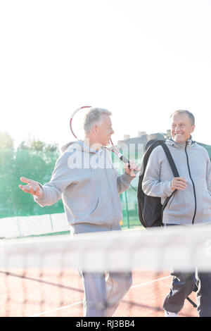 Lächelnde Männer in Sport Kleidung sprechen beim Gehen auf Tennisplatz gegen den klaren Himmel Stockfoto