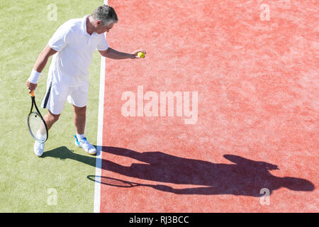 Hohe Betrachtungswinkel und der Zuversichtlichen reifer Mann auf Tennisplatz während des Spiels, das an einem sonnigen Tag Stockfoto