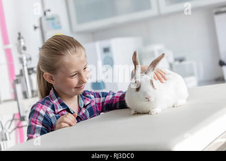 Lächelnde niedliche Mädchen an Kaninchen suchen auf dem Bett in der Tierärztlichen Klinik Stockfoto