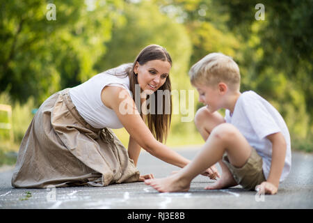 Ein kleiner Junge mit der Mutter Zeichnung hopse auf einer Straße in den Park an einem Sommertag. Stockfoto