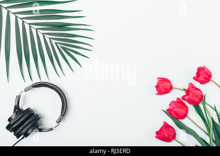 Flach Rahmen der Ohrhörer in der Nähe von Green Palm Leaf und Bouquet von rosa Tulpen auf weißem Hintergrund mit leeren Raum in zentraler Lage. Stockfoto