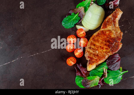 Schweinefleisch Steaks vom Grill mit Gemüse und Gewürzen auf dunklem Stein Hintergrund Stockfoto