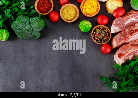 Rohes Fleisch saftige Steaks zum Rösten bereit, verschiedenen Gewürzen, Pfeffer und Kräuter. Platz für Text auf einem schwarzen Brett Hintergrund. Stockfoto