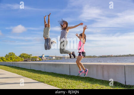 Eine Familie von drei Herausforderung zu sehen, wer die höchste von der Ufermauer auf einem hellen, sonnigen Tag springen können. Stockfoto