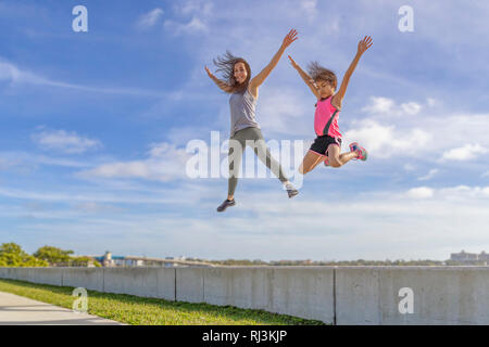 Mutter und Tochter Herausforderung zu sehen, wer die höchste von der Ufermauer auf einem hellen, sonnigen Tag springen können. Stockfoto