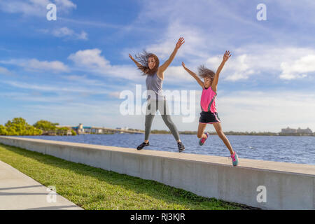 Mutter und Tochter gemeinsam springen von einer ufermauer auf einem hellen, sonnigen Tag. Stockfoto