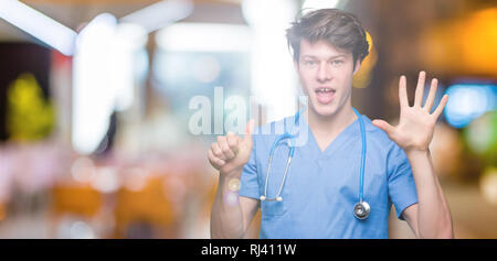 Junger Arzt mit medizinischen gleichmäßig über isolierte Hintergrund angezeigt und zeigen mit den Fingern Nummer sechs, während lächelte zuversichtlich und fröhlich. Stockfoto