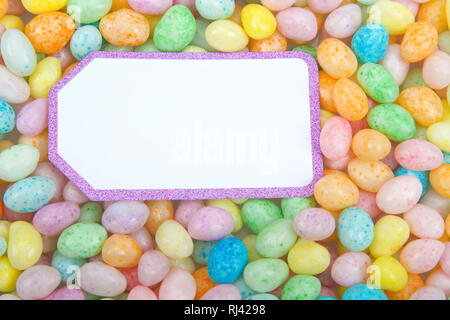 Viele bunte Bonbons Jelly Beans auf flacher Oberfläche, weiße Karte mit funkelnden lila Rand kopieren. Ostern Thema Stockfoto