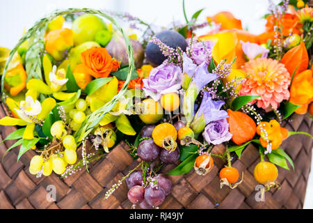 Schöne Dekoration Blumen Zusammensetzung oder Blumenstrauß saisonale Früchte Trauben dogrose Hagebutte und Physalis oder Winter Kirsche mit vielen Blumen orange violett und grün Farbe im Stroh Korb Stockfoto