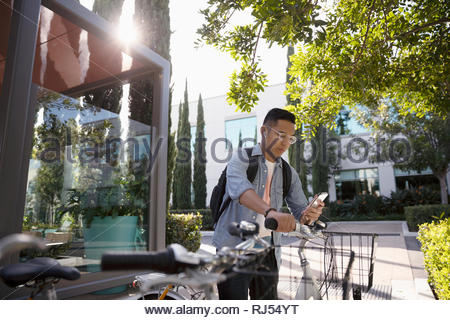 Junger Mann mit Fahrrad mittels Smart Phone auf Bürgersteig