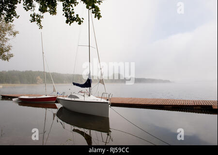 Zwei Boote im Nebel vertäut am See in düsteren Wetter zum Boardwalk, wartet in bewölkten Morgen am Jezioro Powidzkie in Polen, Europa, Herbst, wa Stockfoto