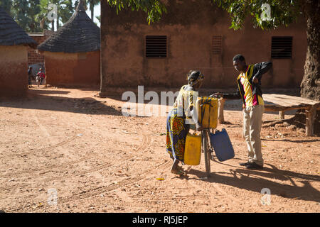 Bodadiougou Village, Banfora, Cascades Region, Burkina Faso, 4. Dezember 2016; EINE Frau, die auf ihrem Fahrrad in ihre Verbindung mit Wasserbehältern zurückkehrt. Stockfoto