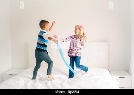 Zwei Kaukasischen cute adorable lustig Kinder springen auf Bett im Schlafzimmer und Spielen. Jungen und Mädchen haben Spaß kämpfen mit Luftballons. Beste Freunde für Stockfoto