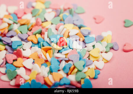 Happy Valentinstag. Haufen von kleinen Süßigkeiten Herzen verschiedener Farben. Ein rotes Herz in der Mitte. Konzept der Liebe und Februar Urlaub. Einsamkeit ein Stockfoto