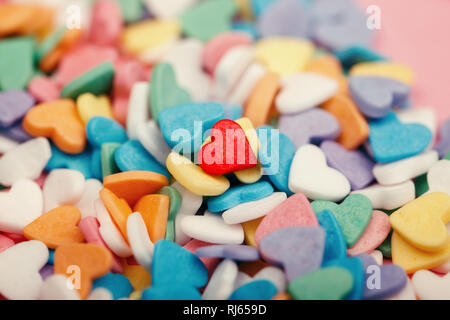 Happy Valentinstag. Haufen von kleinen Süßigkeiten Herzen verschiedener Farben. Ein rotes Herz in der Mitte. Konzept der Liebe und Februar Urlaub. Einsamkeit ein Stockfoto