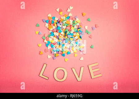 Happy Valentinstag. Schöne Karte mit Haufen von bunten Herzen Bonbons auf Rosa coral Hintergrund. Konzept der Februar Urlaub. Holz- wörter Buchstaben s Stockfoto