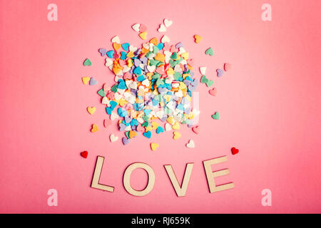 Happy Valentinstag. Schöne Karte mit Haufen von bunten Herzen Bonbons auf Rosa coral Hintergrund. Konzept der Februar Urlaub. Holz- wörter Buchstaben s Stockfoto