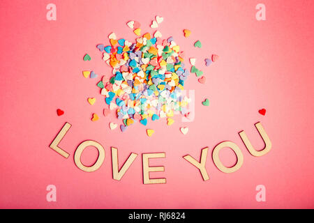 Happy Valentinstag. Schöne Karte mit Haufen von bunten Herzen Bonbons auf Rosa coral Hintergrund. Konzept der Februar Urlaub. Holz- wörter Buchstaben s Stockfoto