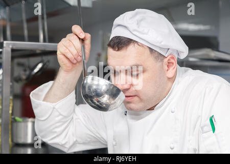 Closeup Portrait man professioneller Koch in weiße Uniform versucht, Teller aus der Küche Pfanne gemacht. Konzept der Qualitätssicherung in das Restaurant, die de Stockfoto