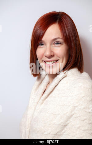 Junge lächelnde rothaarige Mädchen mit Bob Haircut auf gestrickte Pullover beige auf weißem Hintergrund. Konzeption Fotoshooting im Studio Stockfoto