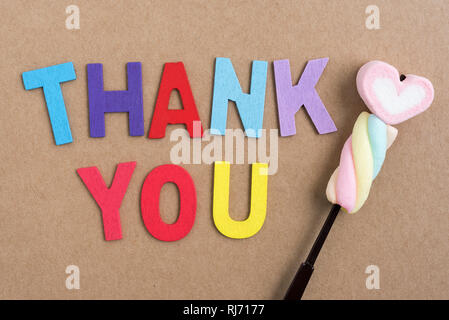 Die bunten Worte danke mit Holzbuchstaben mit Valentine Herzen Bonbons auf braunem Papierhintergrund gemacht Stockfoto