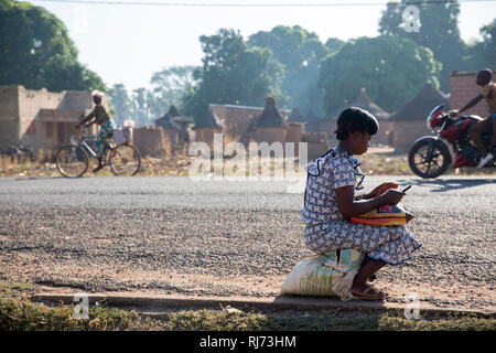 Diarabakoko-Dorf, Banfora, Cascades Region, Burkina Faso, 5. Dezember 2016; EINE Frau kontrolliert ihr Handy am Straßenrand. Stockfoto