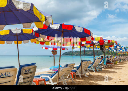 Reihe von Liegestühlen und bunten Sonnenschirmen und Liegestühlen auf der sandigen Küste am Surin Strand, an der Westküste von Phuket, Thailand Stockfoto