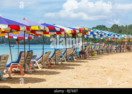Reihe von Liegestühlen und bunten Sonnenschirmen und Liegestühlen auf der sandigen Küste am Surin Strand, an der Westküste von Phuket, Thailand Stockfoto