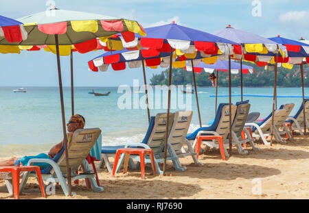 Reihe von Liegestühlen und bunten Sonnenschirmen und Liegestühlen auf der sandigen Küste am Surin Strand, an der Westküste von Phuket, Thailand Stockfoto