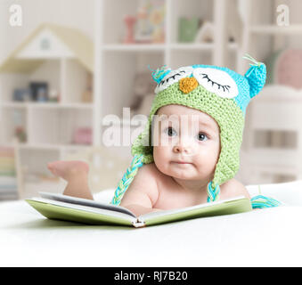 Baby in lustige Eule Strickmütze Eule liegend mit Buch im Kindergarten Stockfoto