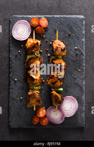 Hühnchen Shish Kebab mit Gemüse auf schwarzem Stein. Ansicht von oben Stockfoto