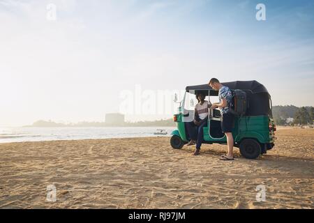 Tuk Tuk Fahrer mit Beifahrer gegen Sand Strand und Meer in Sri Lanka. Stockfoto