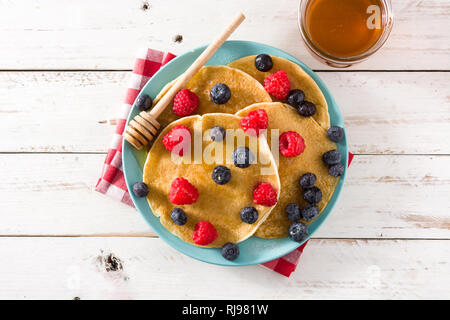 Pfannkuchen mit Himbeeren, Heidelbeeren und Honig auf weiße Holztisch. Ansicht von oben. Stockfoto