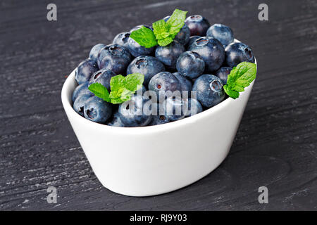 Frische Heidelbeeren in einer weissen Schüssel auf alten schwarzen Holz- Hintergrund (selektive Fokus). Stockfoto