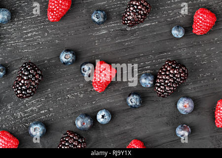 Frische Heidelbeeren, Himbeeren und Brombeeren auf alten schwarzen Holz- Hintergrund, Ansicht von oben (selektive Fokus). Stockfoto