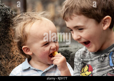 Brüderliche Freude: Zwei junge Brüder teilen sich einen Moment des reinen Glücks, sitzen zusammen mit Vergnügen und Liebe, die in ihren Augen scheint. Stockfoto